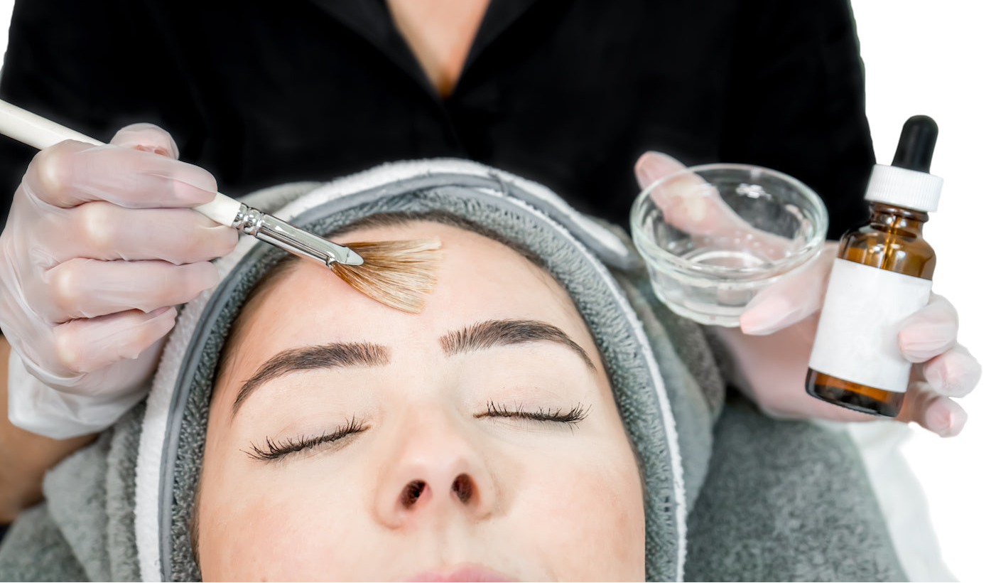 Person receiving a cosmetic procedure with a brush and bottle of liquid.